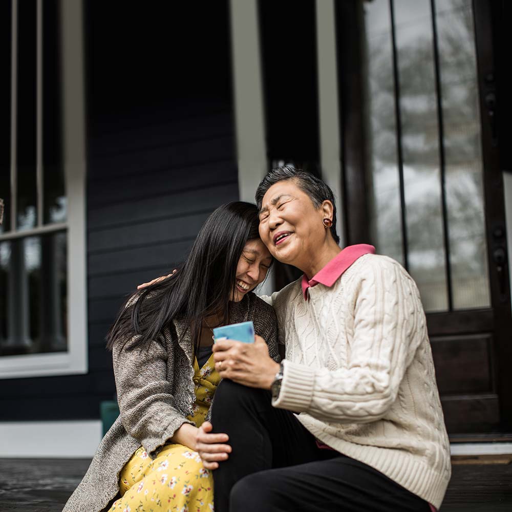 Asian young person and elder embracing and laughing while sitting on porch steps