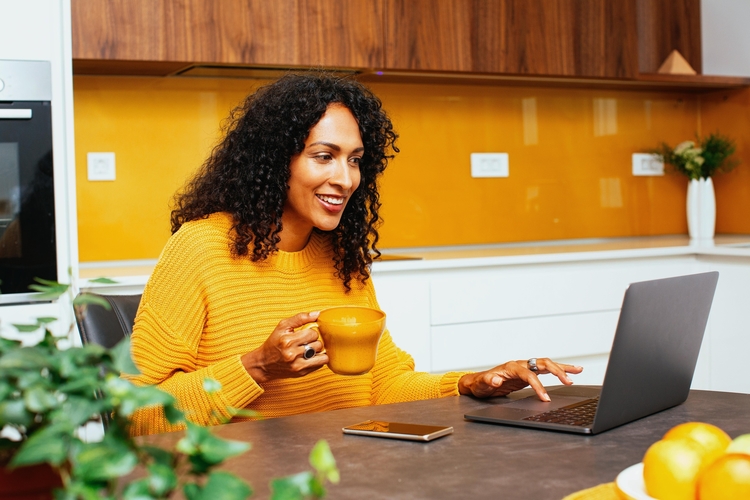 Smiling woman sitting in kitchen with laptop.